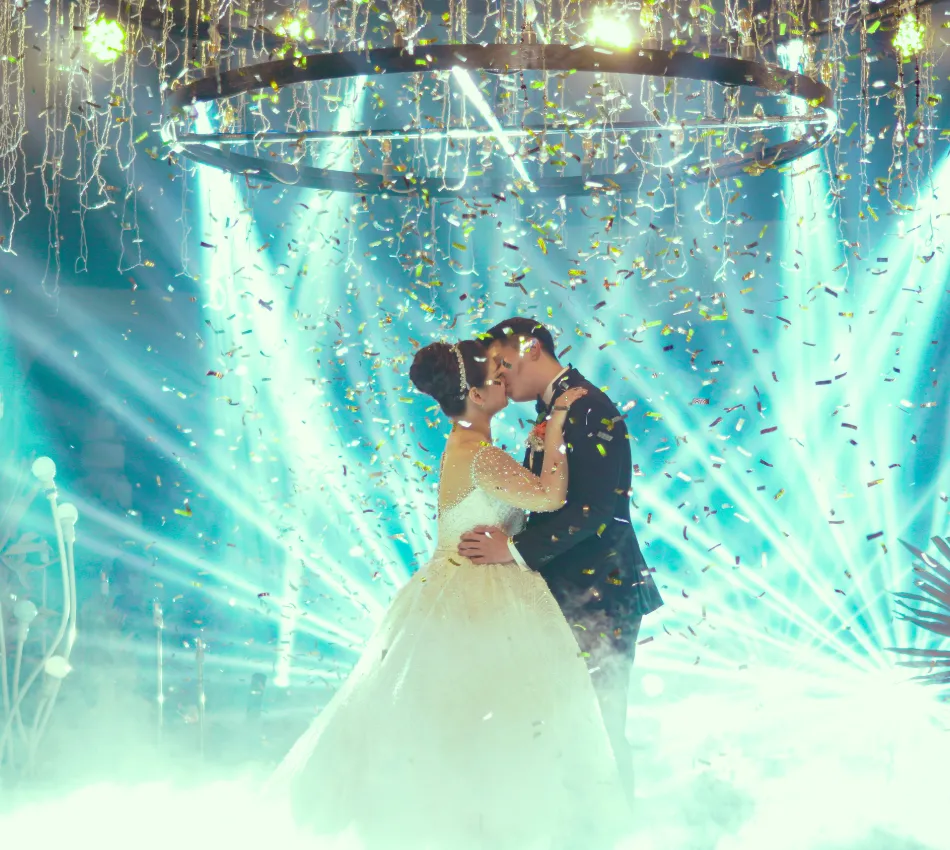 Pareja de novios se besa bajo luces y confeti en su boda.