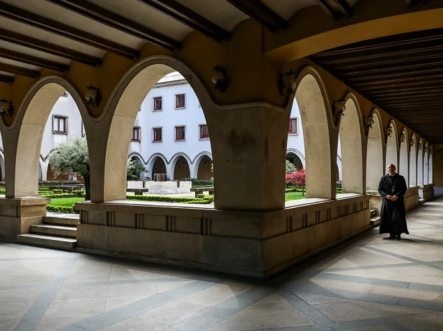 Corredor com arcos e jardim ao fundo, pessoa de roupa preta &agrave; direita.