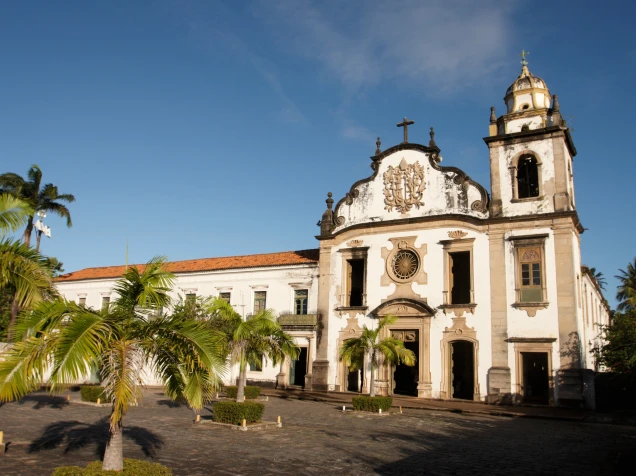 Igreja colonial com palmeiras em destaque sob c&eacute;u azul.