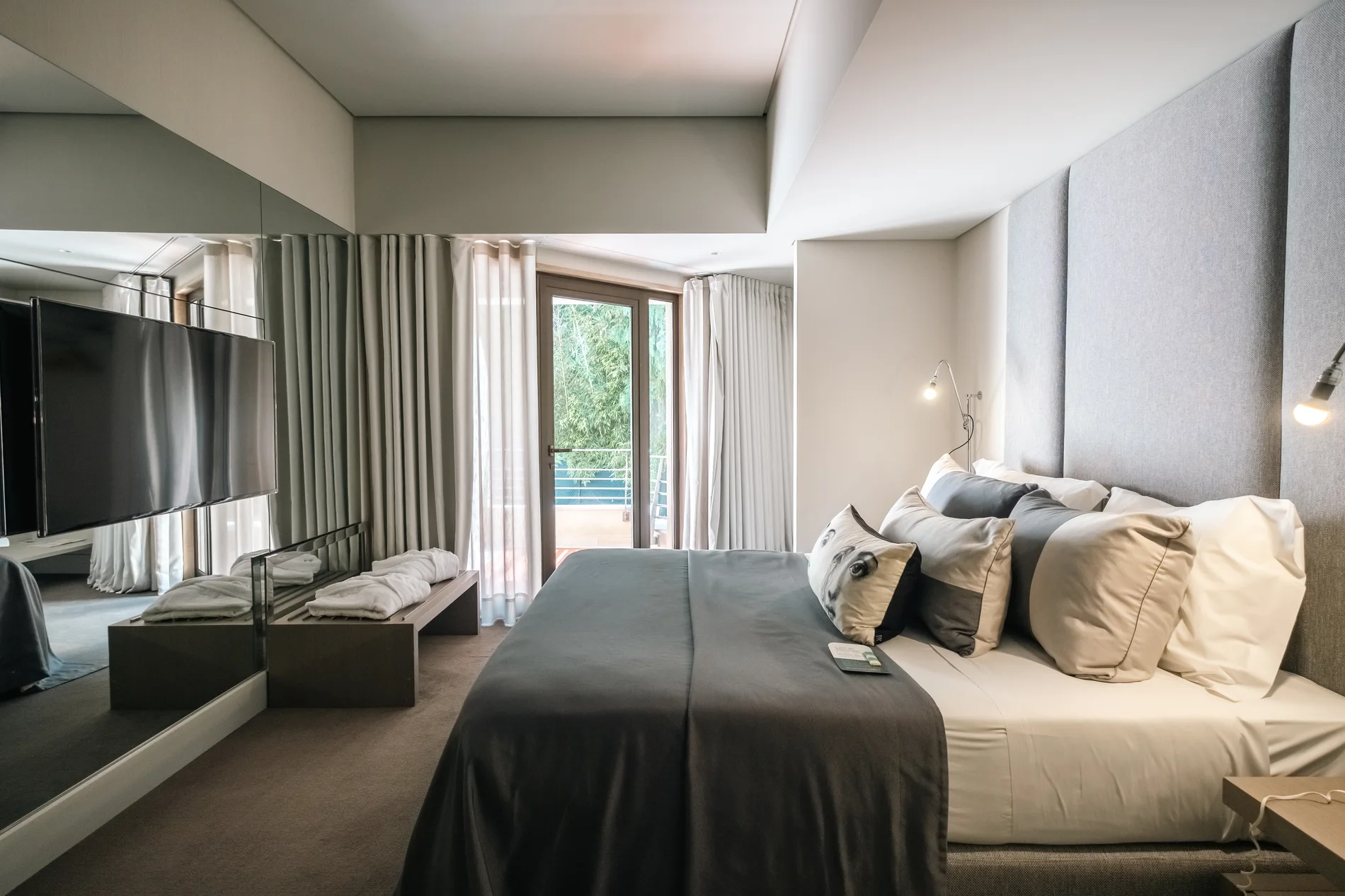 Quarto moderno com cama, TV e cortinas claras.