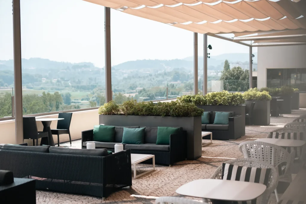 Terra&ccedil;o ao ar livre com sof&aacute;s, mesas e vista para a paisagem verde.