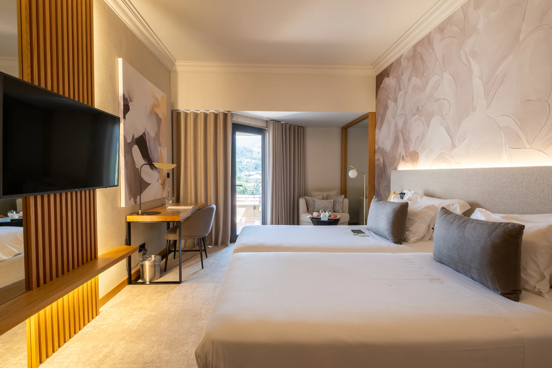 Quarto de hotel moderno com duas camas, mesa e vista para varanda.