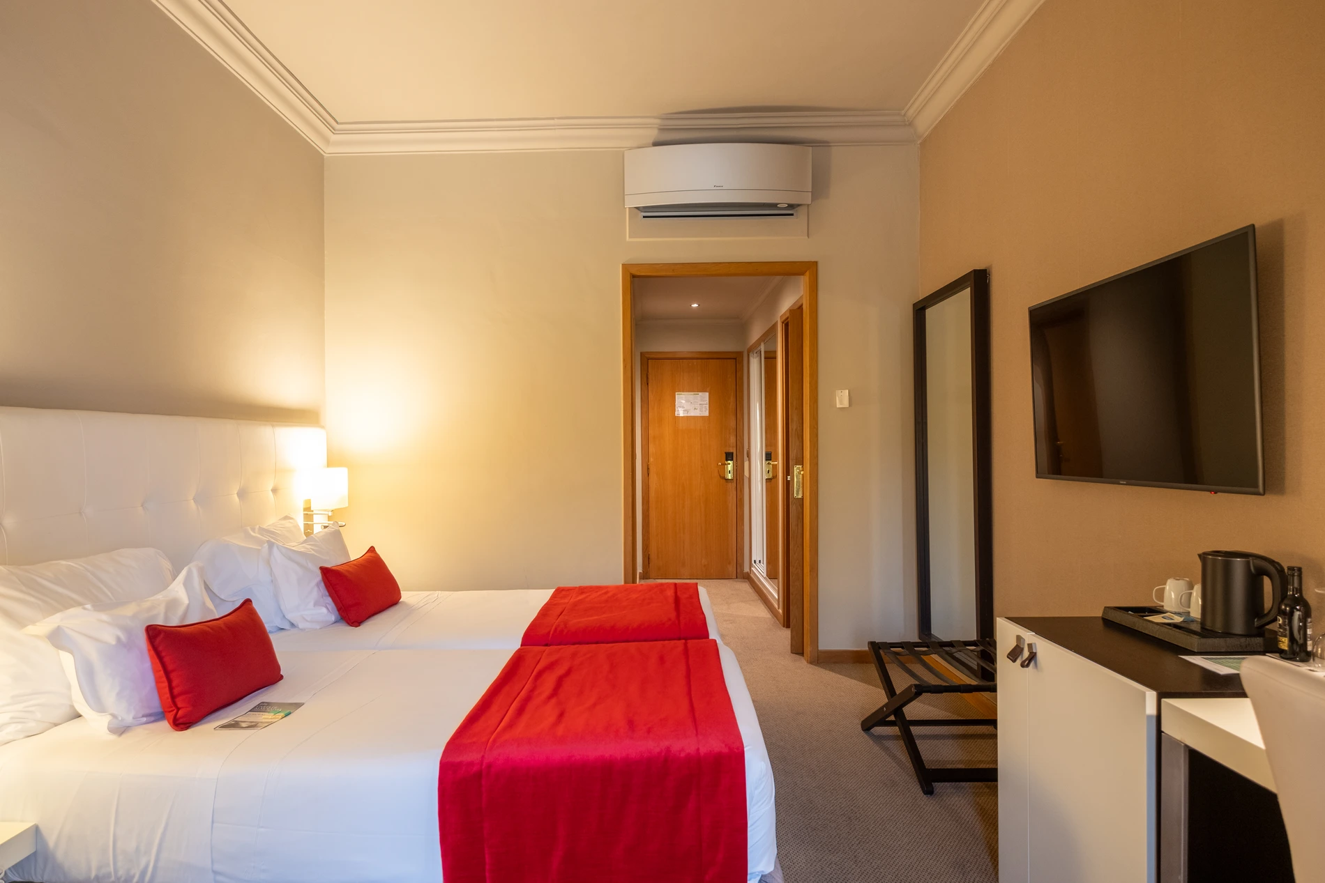 Quarto de hotel com camas de solteiro e decora&ccedil;&atilde;o em vermelho.