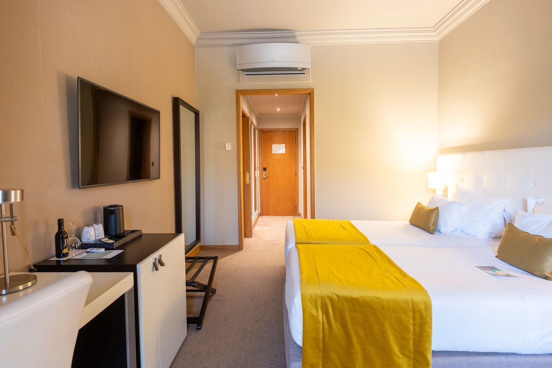 Quarto de hotel com duas camas, TV, mesa e ar-condicionado.