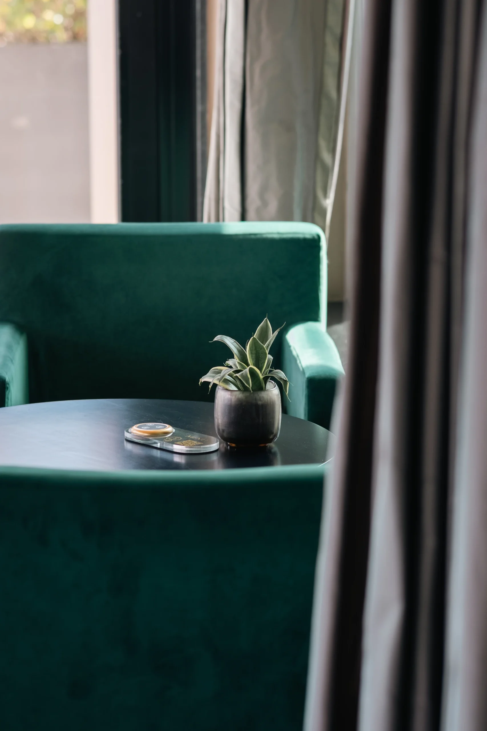 Mesa redonda com planta e controles ao lado de poltrona verde.
