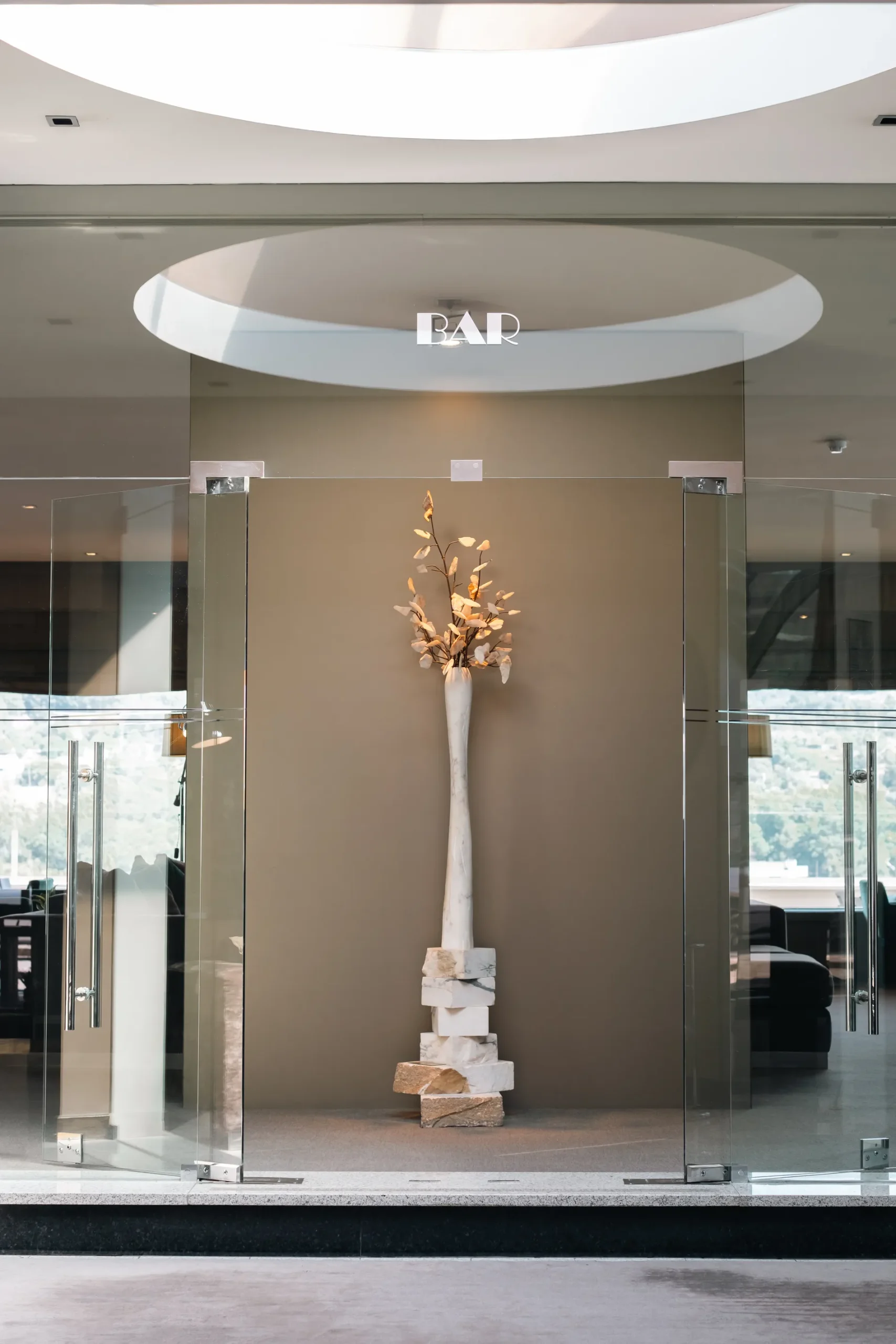 Entrada de bar moderno com escultura e portas de vidro.