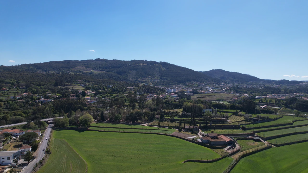 Paisagem rural com campos e colinas sob c&eacute;u azul claro.
