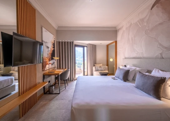 Quarto de hotel moderno com cama grande, TV e vista para montanhas.