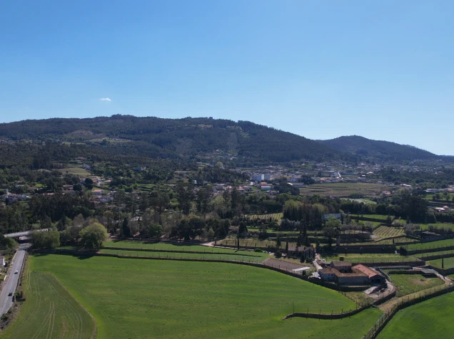 Vista a&eacute;rea de paisagem rural com campos verdes e montanhas ao fundo.