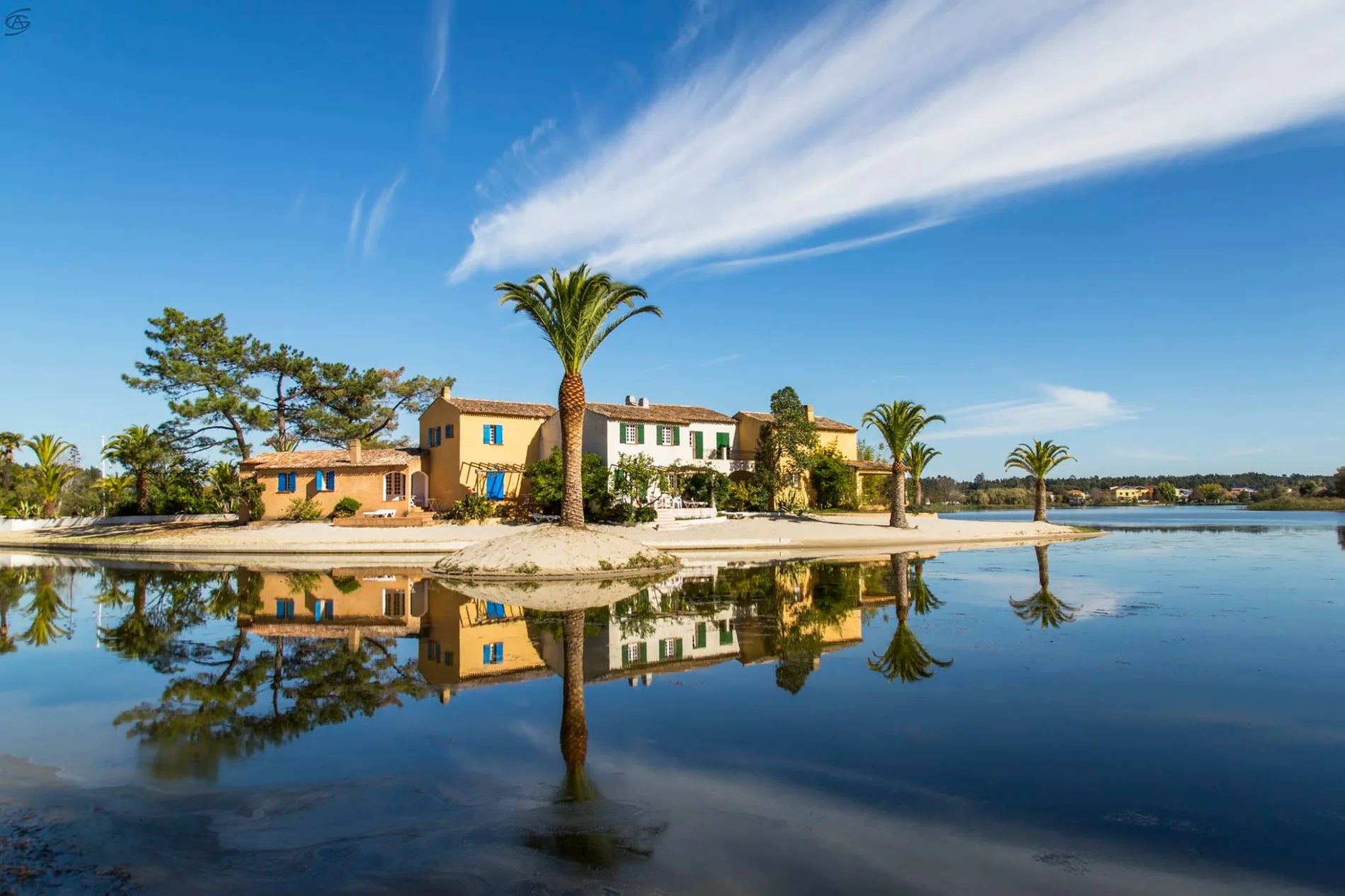 Casa &agrave; beira de um lago, com palmeiras refletidas na &aacute;gua.