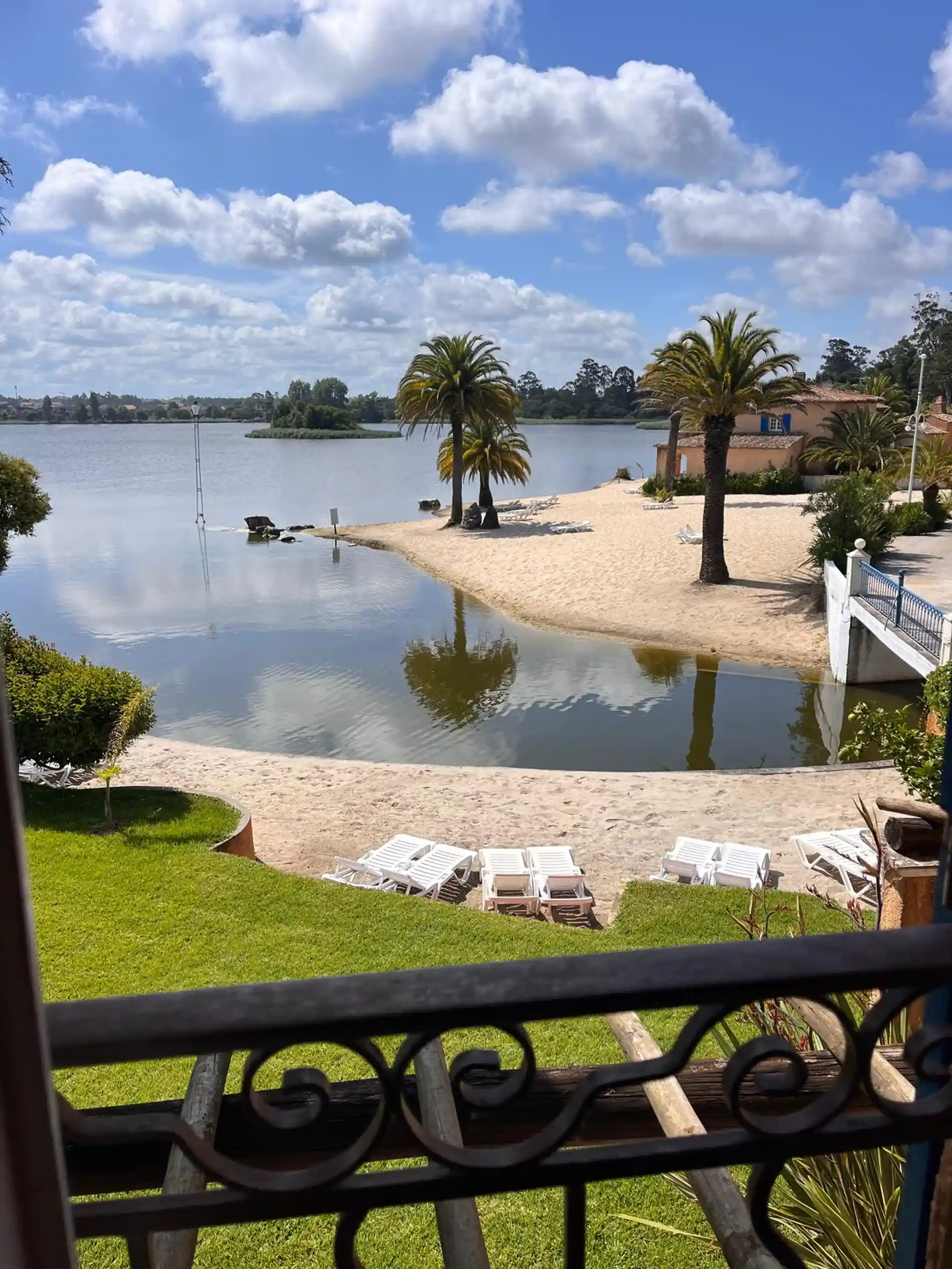 Praia de lagoa com palmeiras, espregui&ccedil;adeiras e c&eacute;u azul com nuvens.