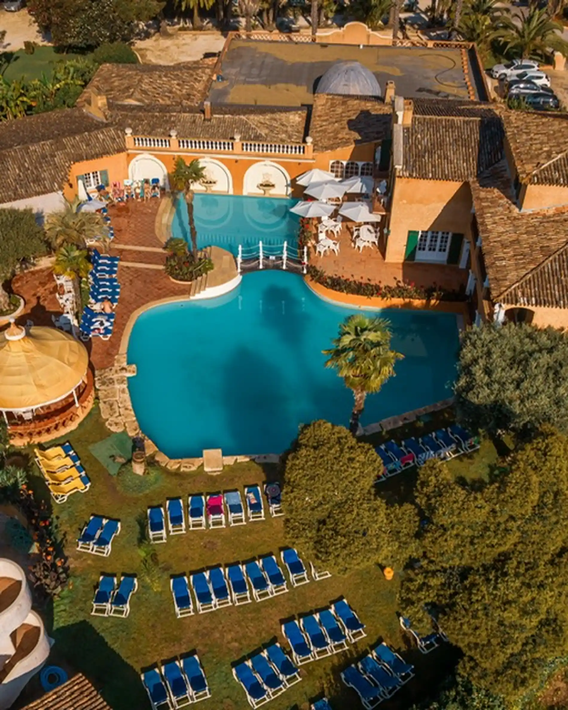 Vista a&eacute;rea de uma piscina em hotel com espregui&ccedil;adeiras e palmeiras.
