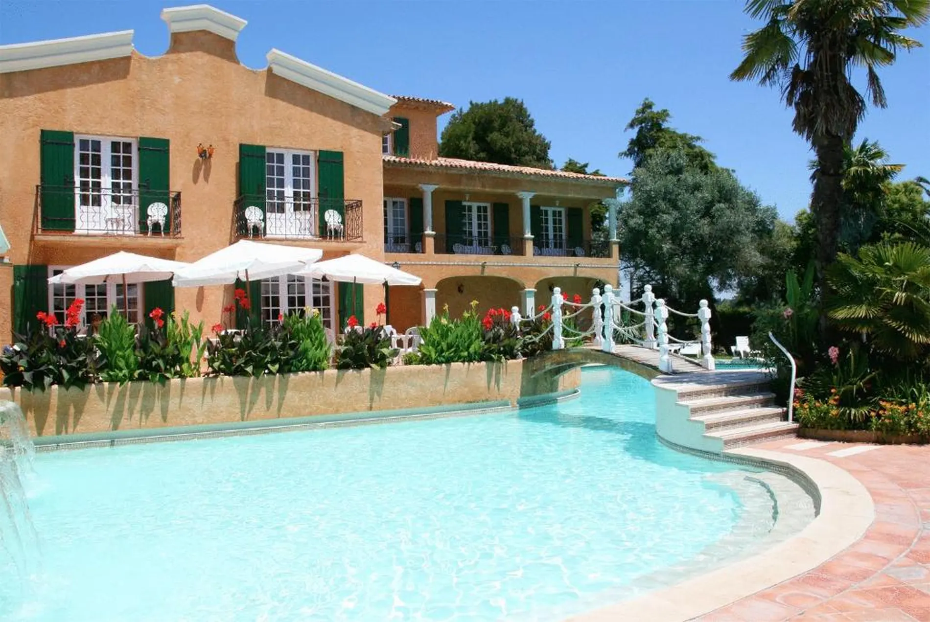 Mans&atilde;o bege com piscina e jardim exuberante ao redor.