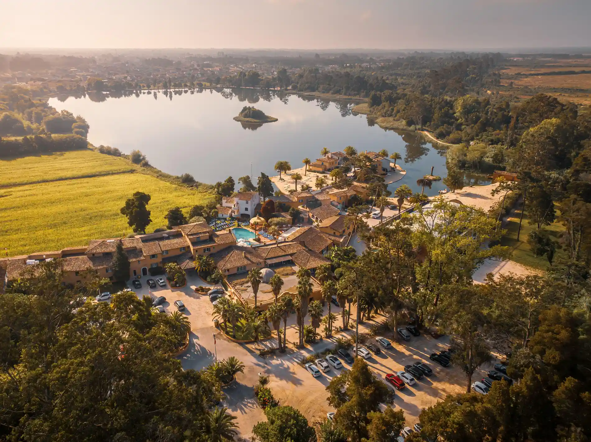 Vista a&eacute;rea de um resort &agrave; beira do lago cercado por &aacute;rvores e &aacute;reas rurais.