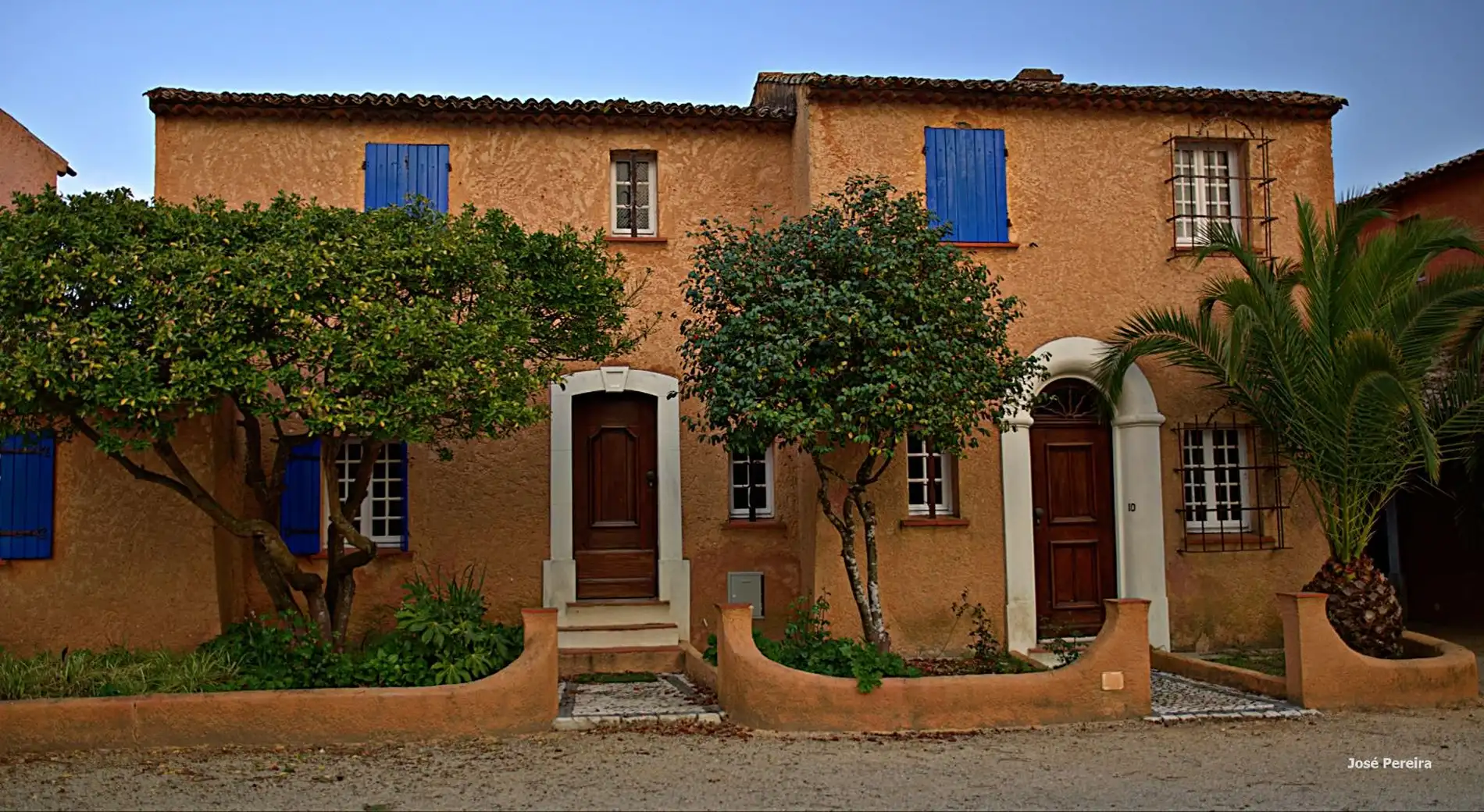Casas de fachada laranja com janelas azuis e &aacute;rvores na frente.