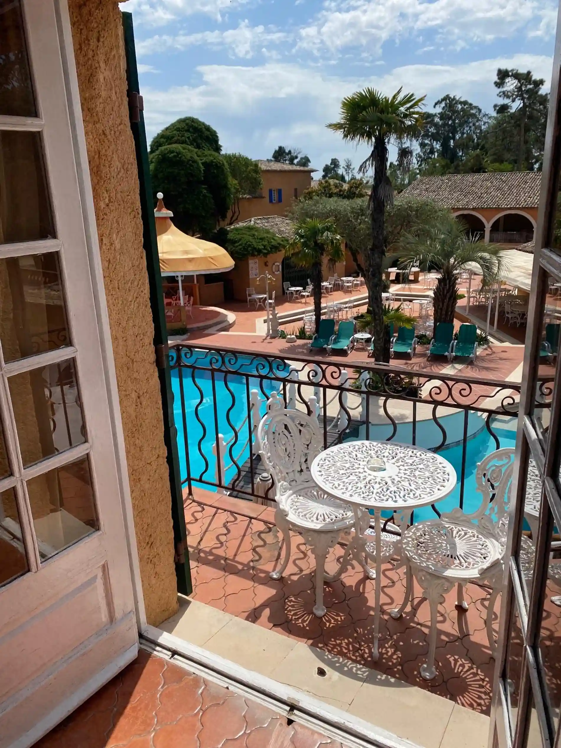 Varanda com mesa e cadeiras de ferro, vista para piscina e jardim.