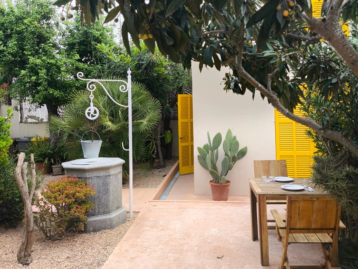 Patio con fuentes, cactus y mesa de madera junto a paredes amarillas y verdes