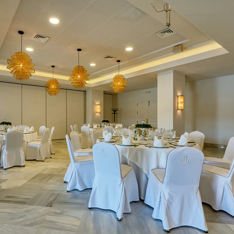 Sala de eventos con mesas vestidas y l&aacute;mparas colgantes de mimbre.