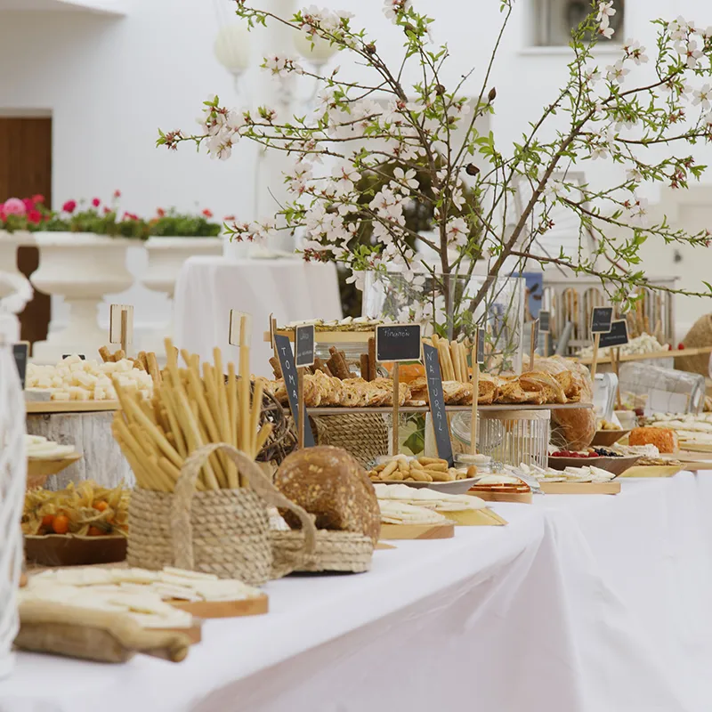 Mesa de buffet con panes y tarjetas, decorada con flores blancas en un evento.