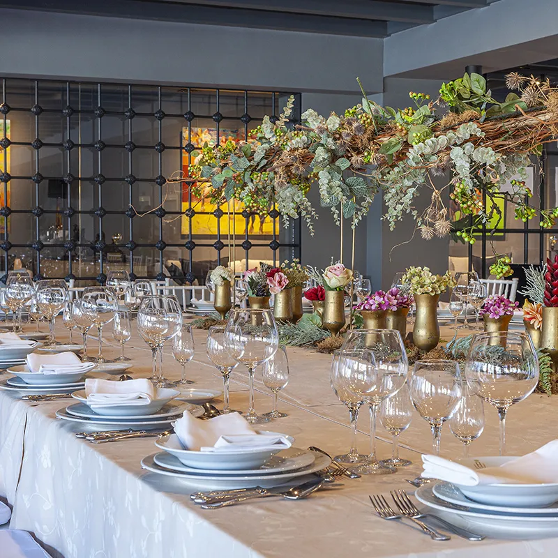 Mesa de banquete con copas y centros florales en interior elegante.