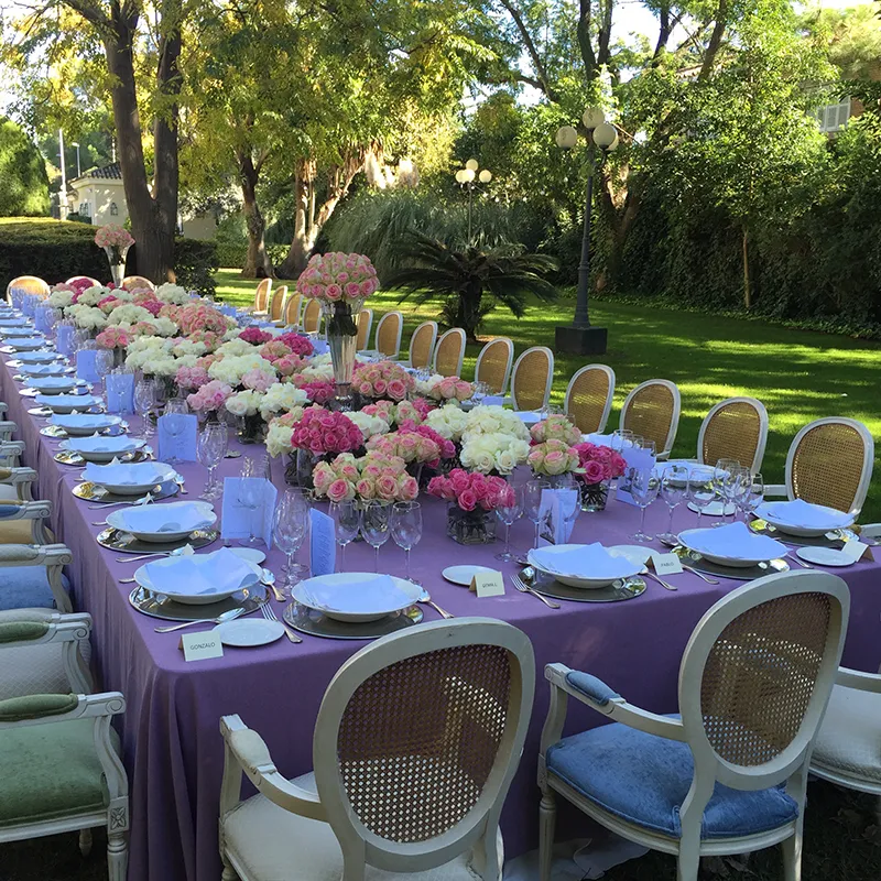 Mesa de banquete al aire libre con arreglos florales y sillas blancas en jard&iacute;n