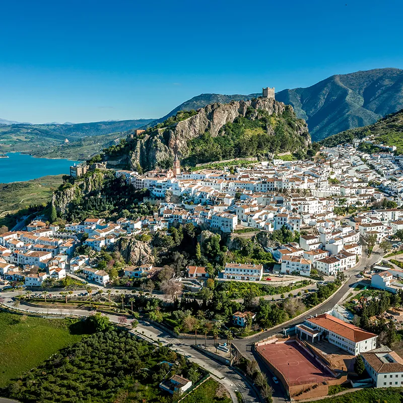 Pueblo blanco en la ladera, con castillo y puerto fluvial entre monta&ntilde;as.