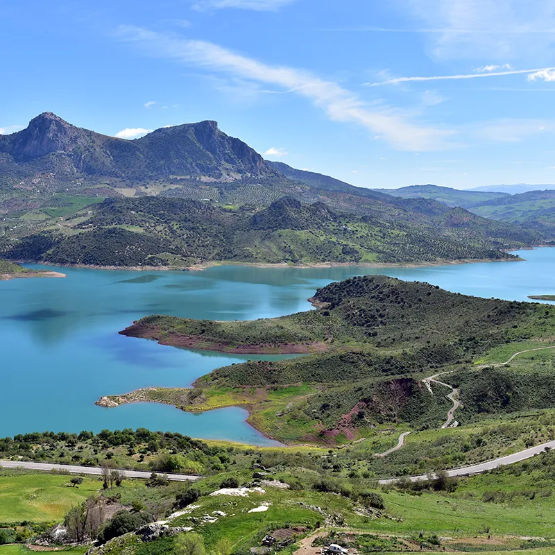 Lago turquesa entre monta&ntilde;as, carreteras y praderas verdes al atardecer