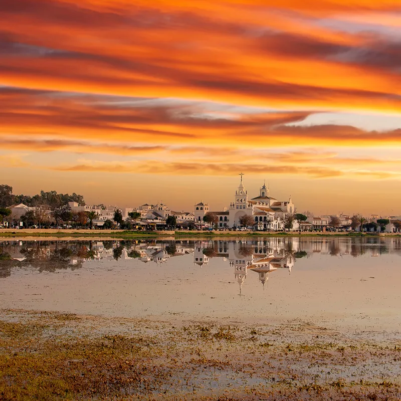 Atardecer con iglesia y reflejo en el lago, cielo naranja y nubes.