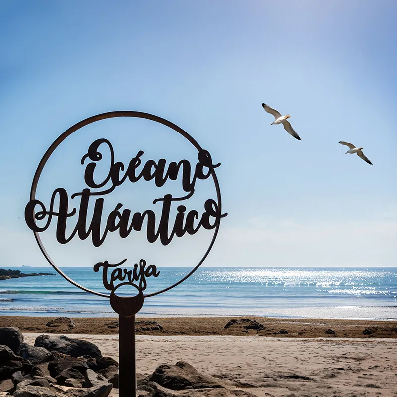 Playa con rocas, gaviotas y letrero &ldquo;Oc&eacute;ano Atl&aacute;ntico Tarfia&rdquo; en un poste.