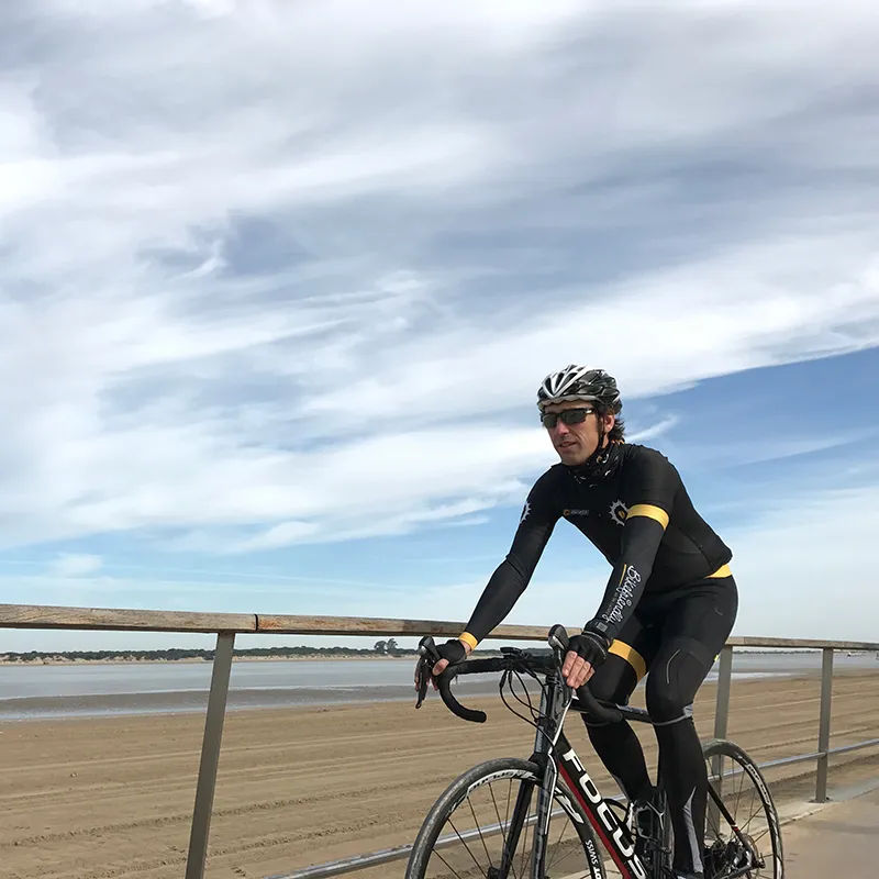 Ciclista con casco y bicicleta, junto a una baranda, en la playa.
