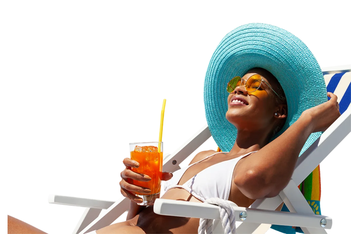 Mujer bajo sombrero azul con gafas, bebiendo bebida naranja en la playa