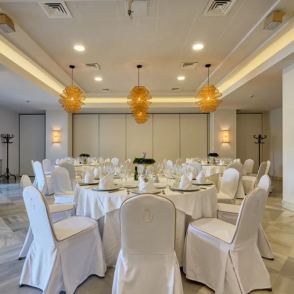 Comedor de banquete con mesas cubiertas y sillas blancas iluminadas.