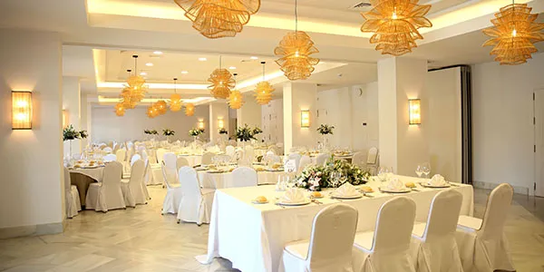 Sal&oacute;n de banquete con mesas blancas y l&aacute;mparas colgantes decorativas doradas