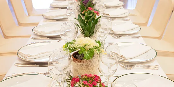 Mesa de banquete con flores y vajilla blanca, copas y arreglos florales.