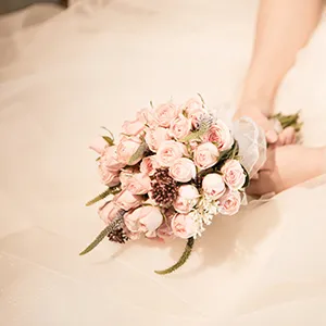 Ramo de rosas rosadas en manos de una novia con velo y flores verdes.