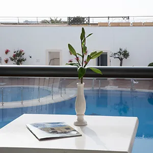 Flor blanca en jarr&oacute;n junto a piscina azul y mesa blanca en terraza