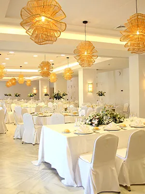 Sal&oacute;n de banquete decorado con l&aacute;mparas colgantes y mesas con mantel blanco