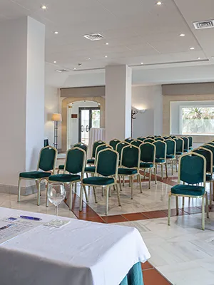 Sala de conferencias con filas de sillas verdes y mesa cubierta con manteles