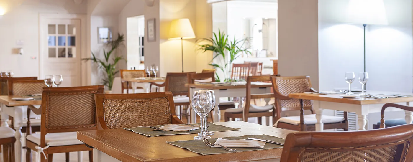 Comedor luminoso con mesas puestas y copas de vino, ambiente acogedor.