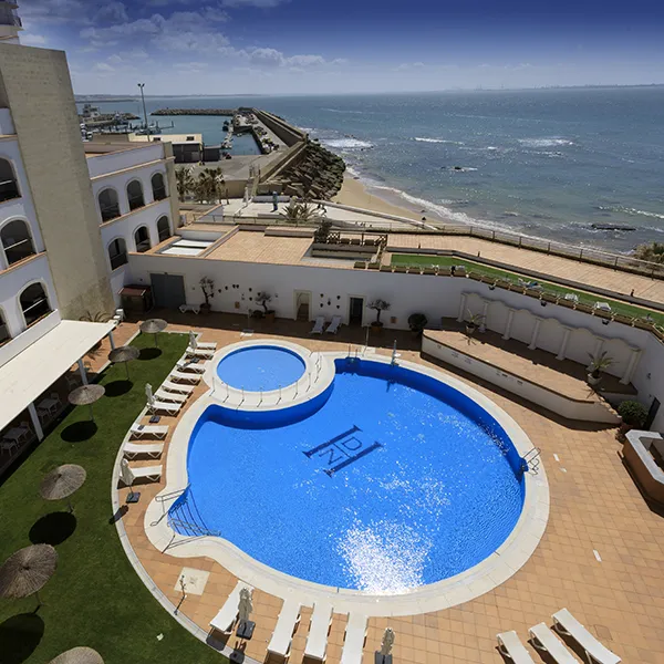 Piscina azul en hotel frente al mar con vista al litoral y cielo despejado.