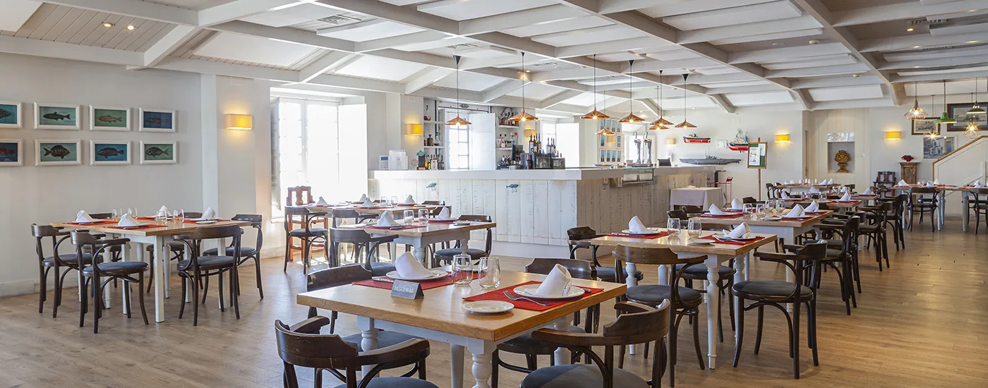 Comedor de restaurante con mesas puestas y bar al fondo, ambiente luminoso