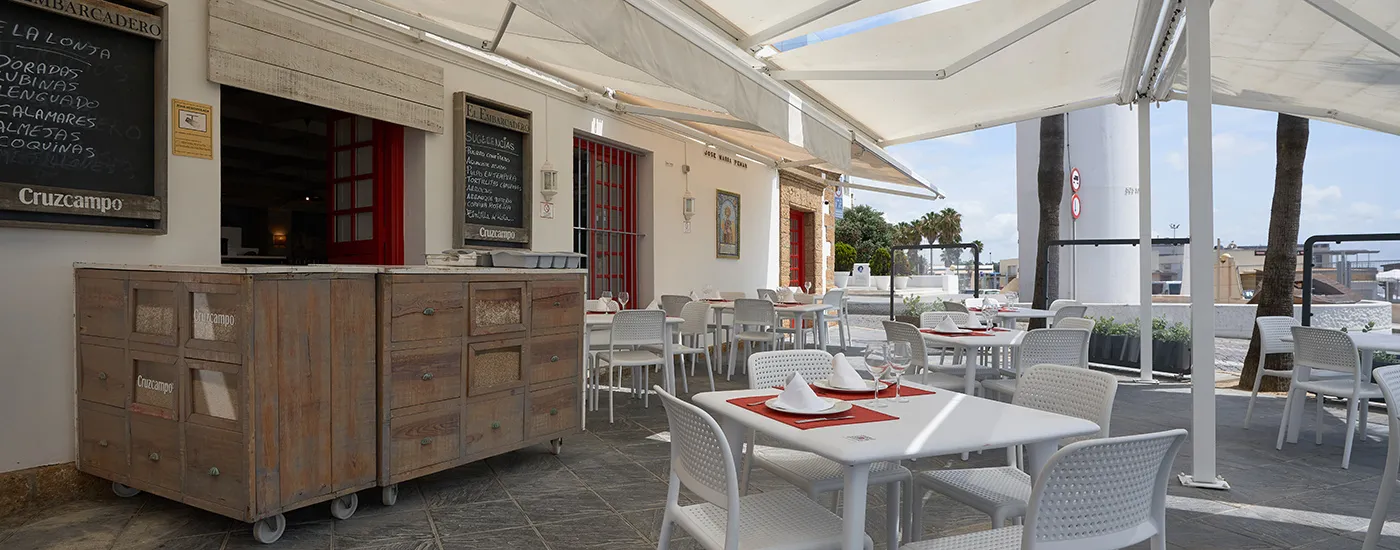 Terraza con mesas y sillas bajo carpa, decoraci&oacute;n de bar y bebidas Cruzcampo