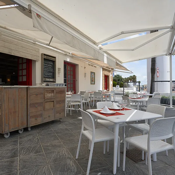 Terraza con mesas y sillas blancas bajo un toldo, al aire libre.