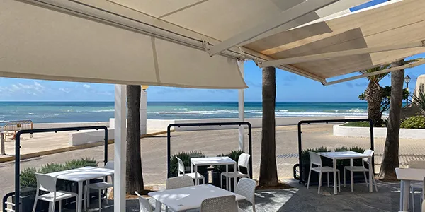 Terraza junto al mar con mesas y sillas bajo p&eacute;rgola blanca