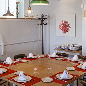 Comedor con mesa servida y l&aacute;mparas colgantes, decoraci&oacute;n marina y coral.