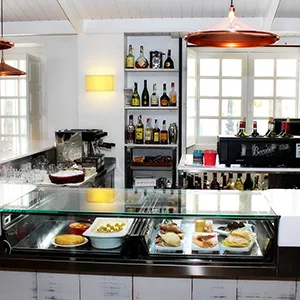 Interior de restaurante con vitrina de comida, mesas y estanter&iacute;a de bebidas
