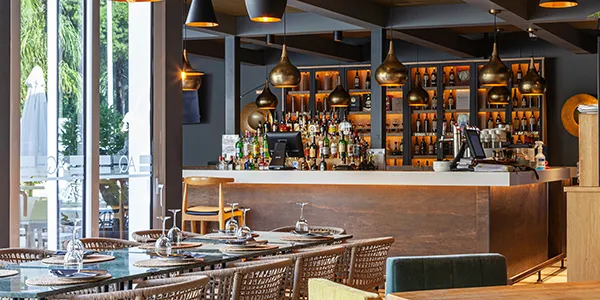 Bar con mesa preparada y barra iluminada con botellas y l&aacute;mparas colgantes.