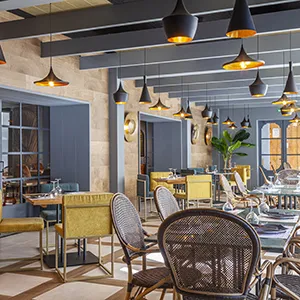 Comedor al aire libre con mesas y sillas, luces colgantes y plantas.