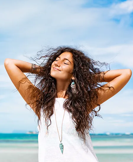 Mujer con los brazos abiertos sonriendo en la playa, al aire libre.
