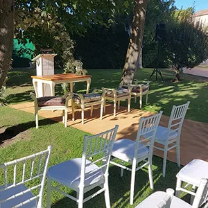 Patio con sillas y mesas blancas y verdes, &aacute;rboles y c&eacute;sped al fondo.